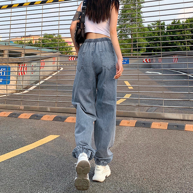 Person wearing light blue jeans and white sneakers standing in a parking lot.