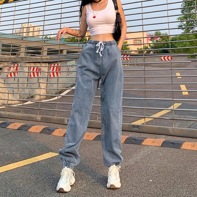 Person wearing a white crop top and blue jeans standing on a street with a metal fence and buildings in the background.
