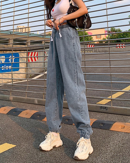 Person wearing light blue jeans and white sneakers on a road with barriers and signs in the background.