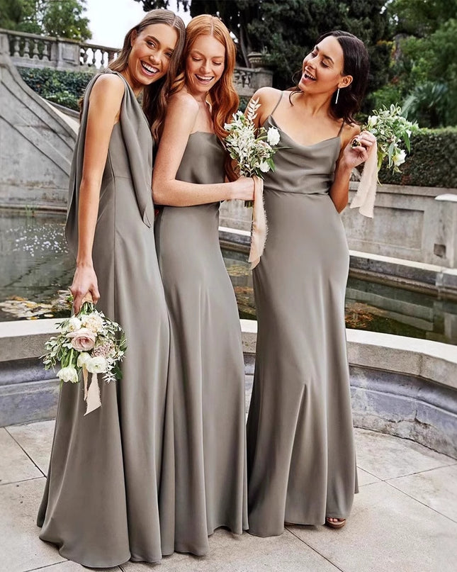 Three women in long, light gray dresses standing outdoors near a stone wall and water feature.
