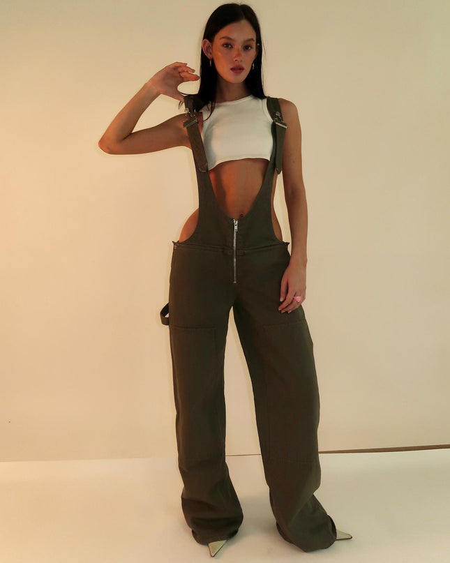 Person wearing brown overalls with a white top on a plain background