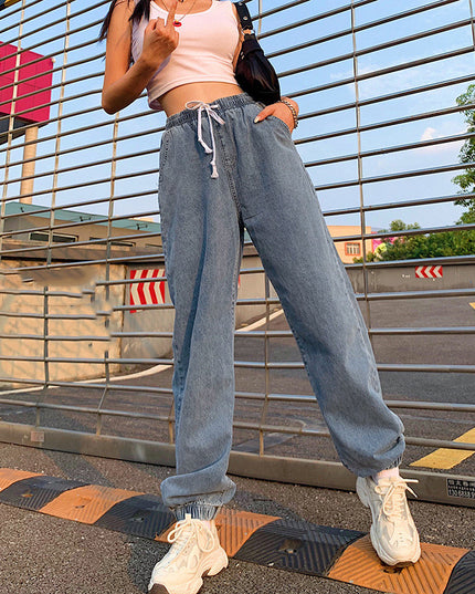 Person wearing a pink crop top and blue jeans standing on a road with a metal gate and 'OK' sign in the background.
