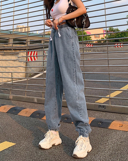 Person wearing light blue jeans and white sneakers on a road with a metal barrier in the background.