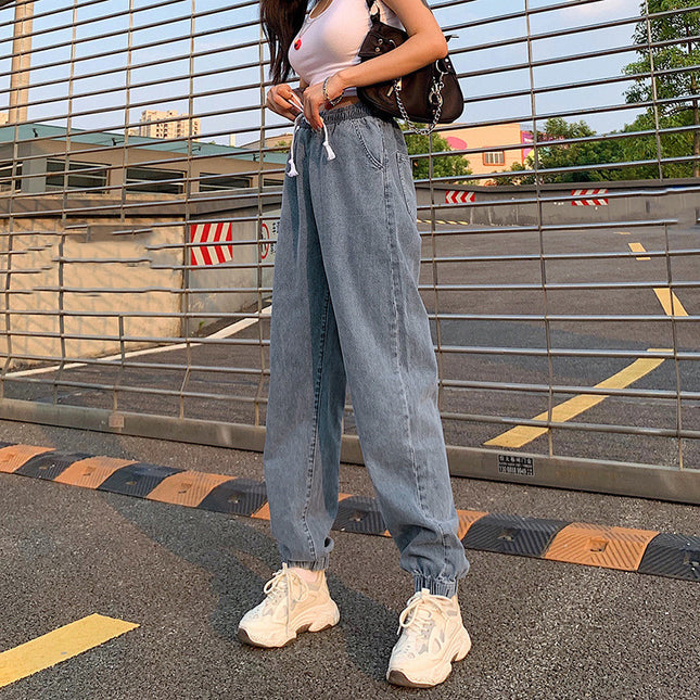 Person wearing light blue jeans and white sneakers on a road with a metal barrier in the background.