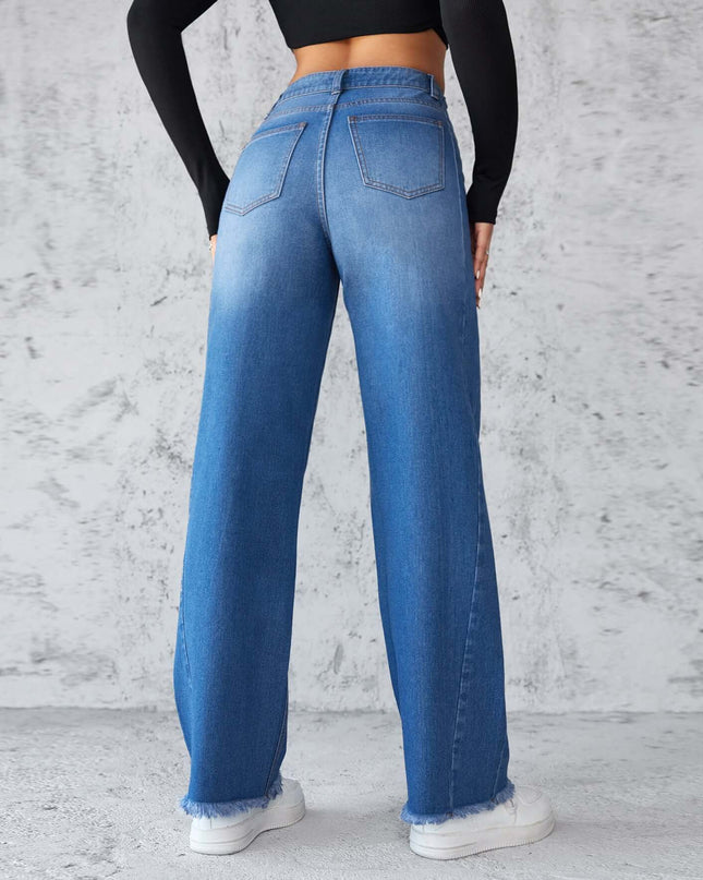 Person wearing blue jeans and a black long-sleeve top against a gray concrete wall.