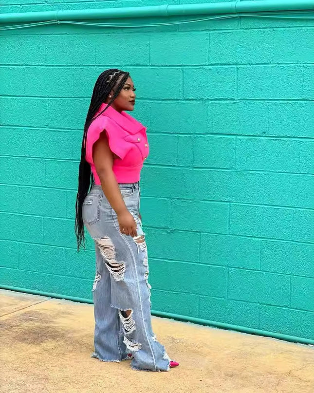 Person wearing a bright pink top and ripped jeans standing against a teal brick wall.
