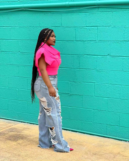 Woman wearing a bright pink top and ripped jeans against a teal brick wall.