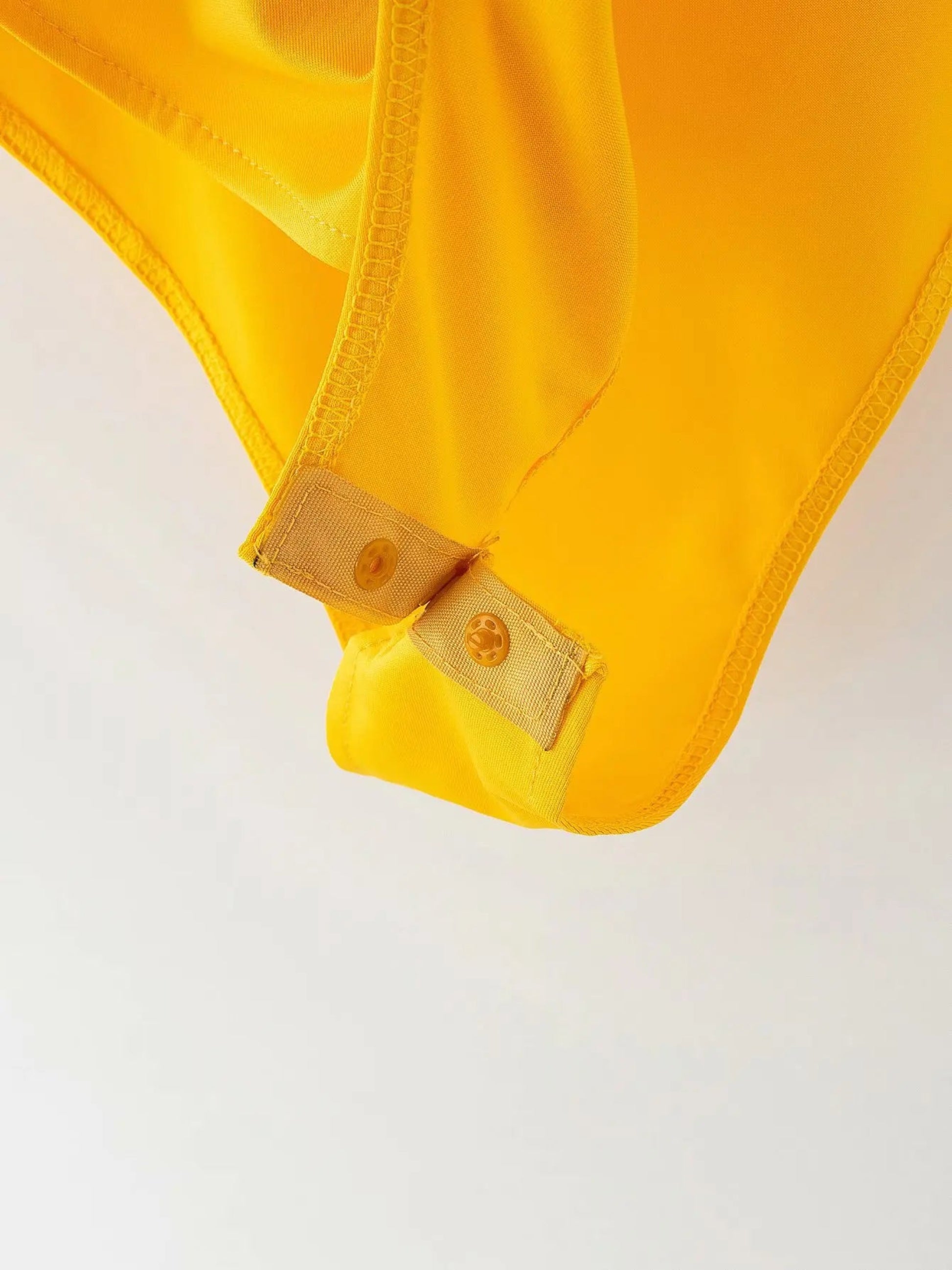 Close-up of a yellow garment with a button on a light gray background