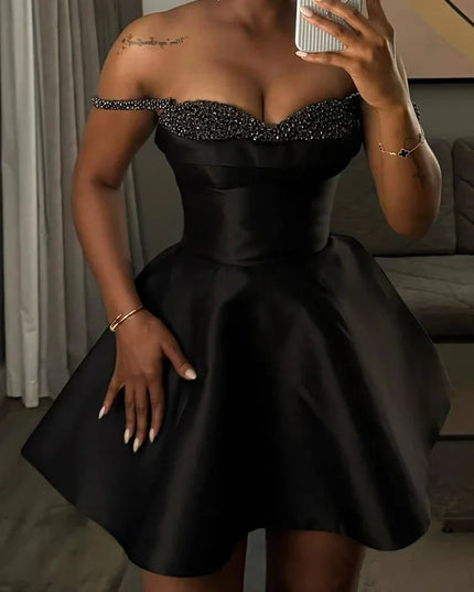 Woman wearing a black dress with a beaded neckline, taking a mirror selfie.