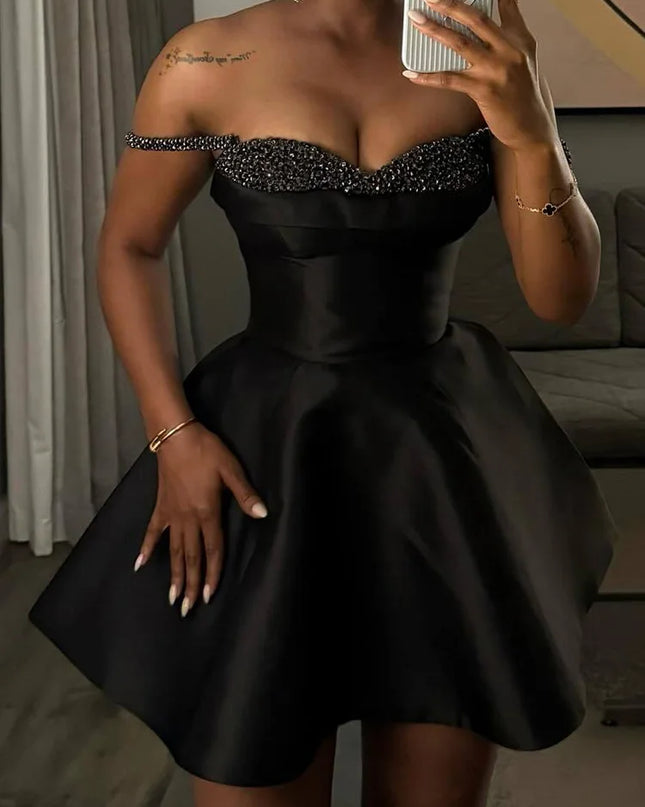 Woman wearing a black dress with a beaded neckline, taking a mirror selfie.