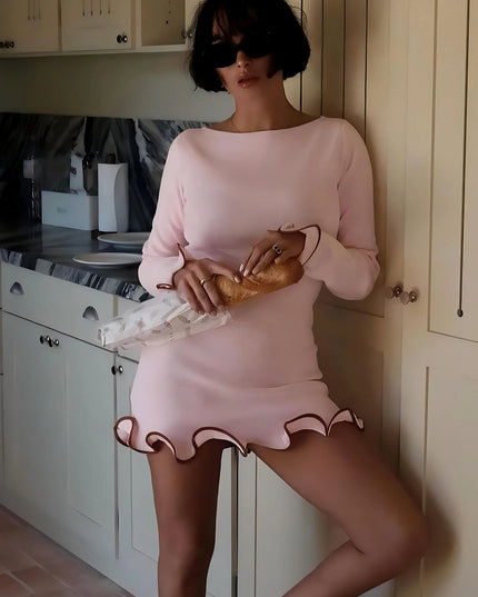 Woman in pink ruffled bodycon mini dress with long sleeves, stylishly posing in a kitchen setting.