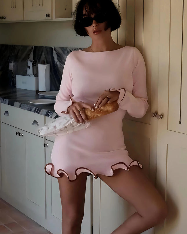 Woman in pink ruffled bodycon mini dress with long sleeves, stylishly posing in a kitchen setting.