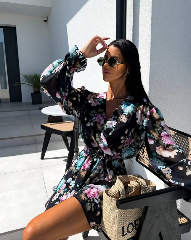 Woman in a floral dress sitting outdoors with sunglasses on, holding a bag.