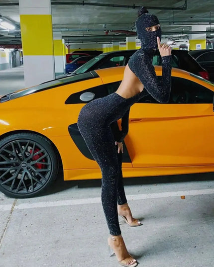 Person in a black outfit and balaclava leaning against a yellow sports car in a parking garage.