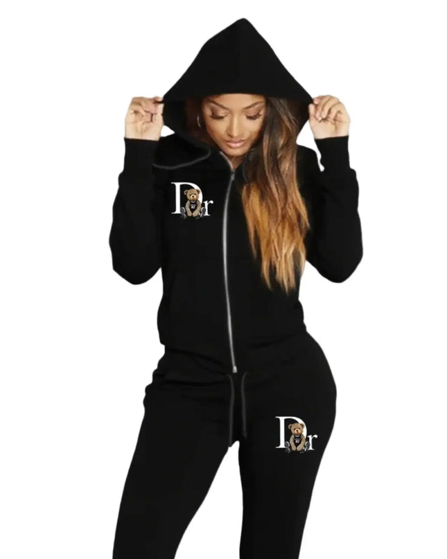 Person wearing a black hoodie and matching pants with a logo on a gray background