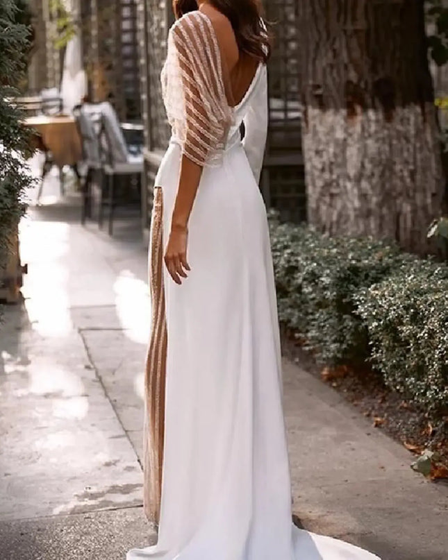 Elegant white dress with sheer lace sleeves, showcasing a deep V-back in a beautiful outdoor setting.