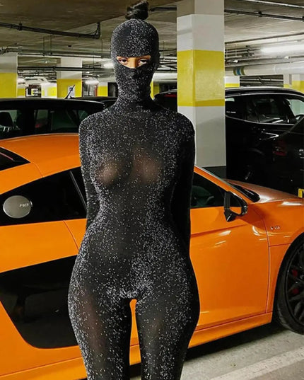 Person wearing a black, sparkly bodysuit in a parking garage with an orange car.