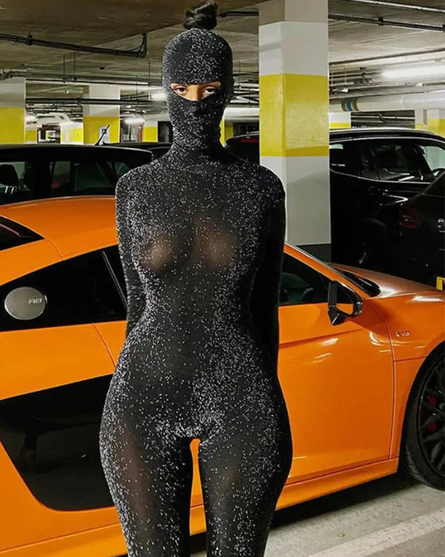Person wearing a black, sparkly bodysuit in a parking garage with an orange car.