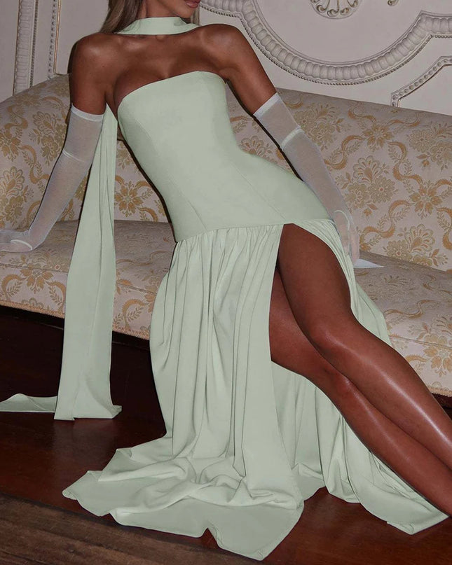 Woman in a light green evening gown with a high slit, standing in an elegant interior setting.