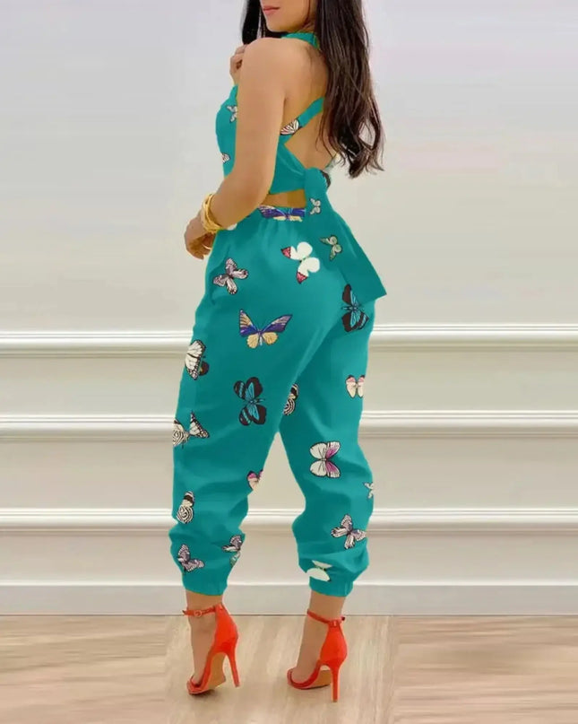 Woman wearing a teal jumpsuit with butterfly patterns against a light-colored wall.