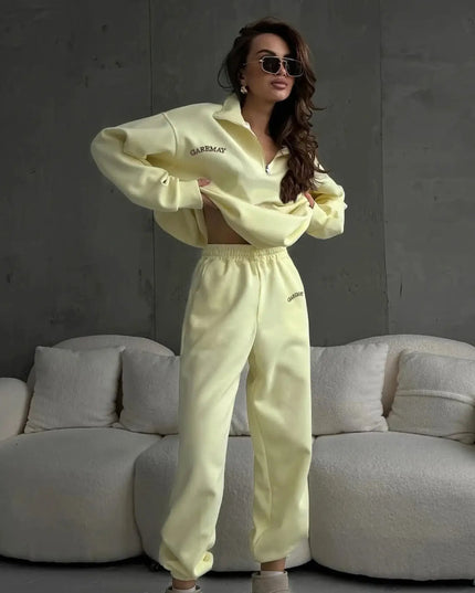 Woman wearing a light yellow tracksuit with sunglasses in a room with a gray sofa.
