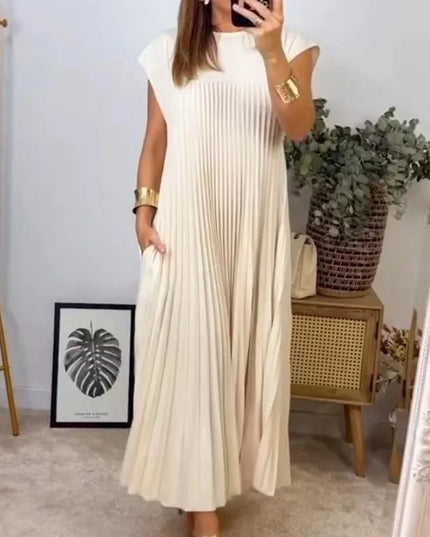 Women’s elegant sleeveless dress with pockets in beige, flowy and pleated design, showcased in a stylish home setting.