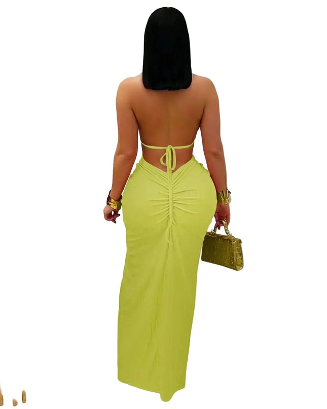 Woman wearing a bright green dress with cut-out back, holding a matching handbag indoors.