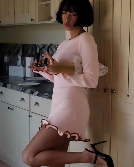 Womens bodycon mini dress in pink featuring ruffled hem and long sleeves, stylishly posed in a kitchen setting.