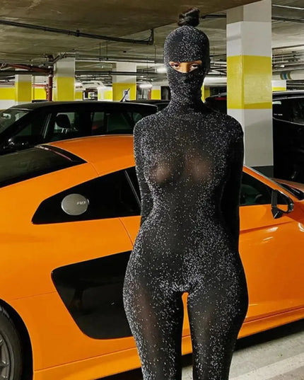 Person wearing a black bodysuit with glitter in a parking garage with an orange car.