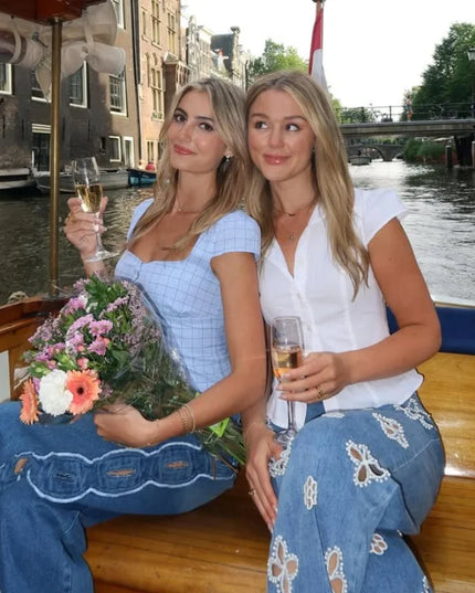 Two women enjoying a boat ride, wearing casual hollow out women’s jeans, holding drinks and flowers.