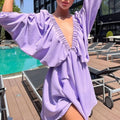 Model wearing a lavender deep V-neck pleated dress with long sleeves by a poolside.