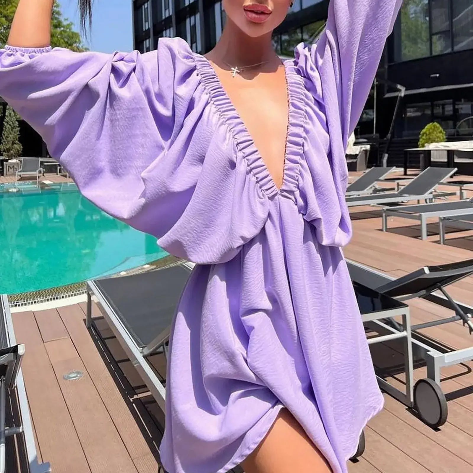 Model wearing a lavender deep V-neck pleated dress with long sleeves by a poolside.