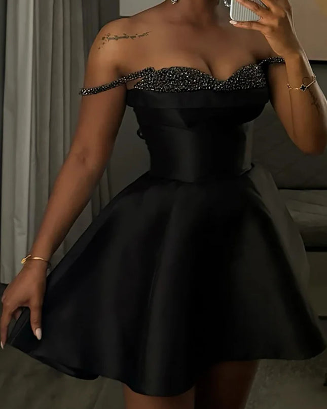 Woman wearing a black off-shoulder dress with embellishments, standing indoors.