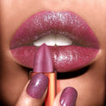 Close-up of a hand holding a purple glittery lipstick against a matching background