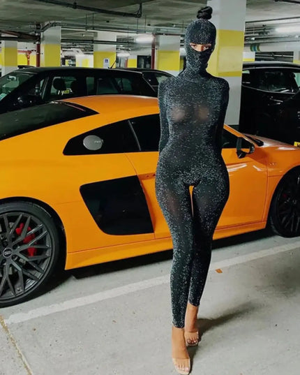 Person in a black glittery outfit standing in a parking garage with an orange sports car.