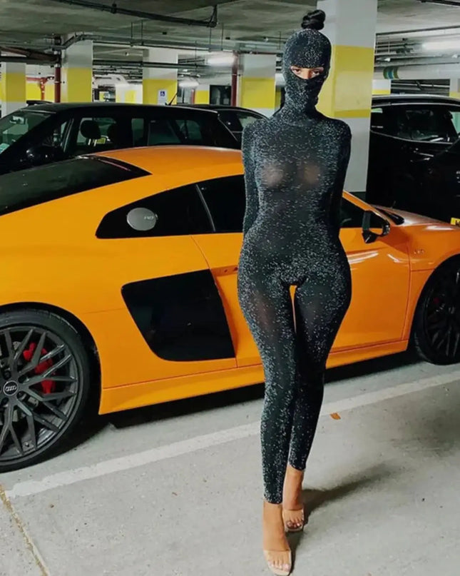 Person in a black glittery outfit standing in a parking garage with an orange sports car.