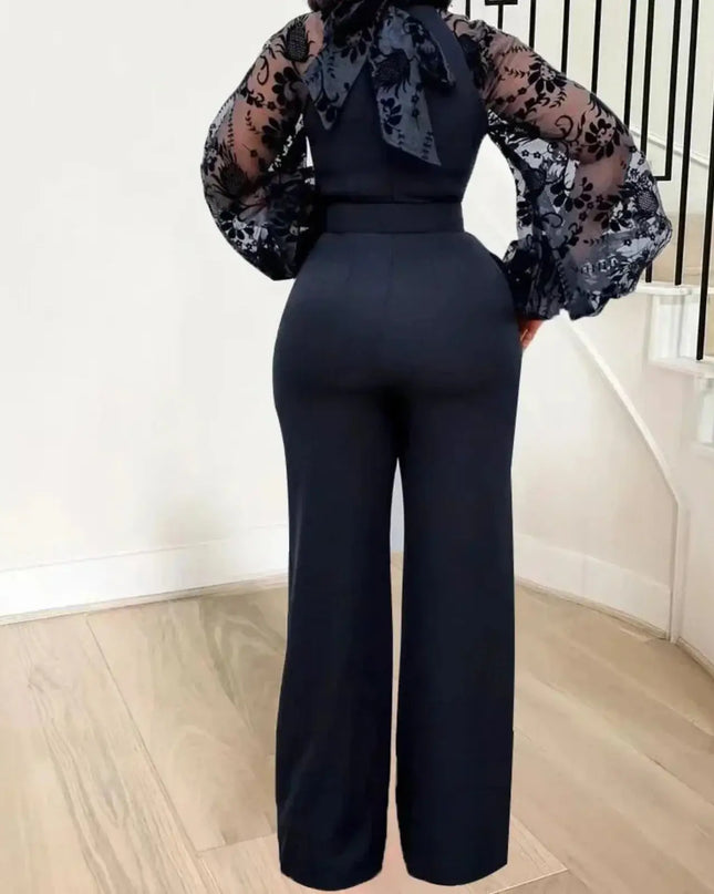 Person wearing a navy jumpsuit with sheer sleeves and floral patterned top in an indoor setting.