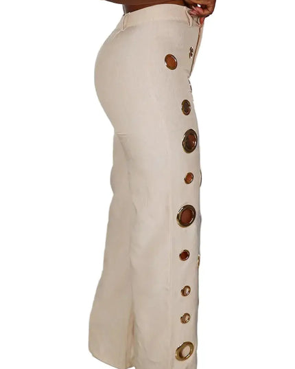 Beige pants with decorative buttons worn by a person against a white curtain background