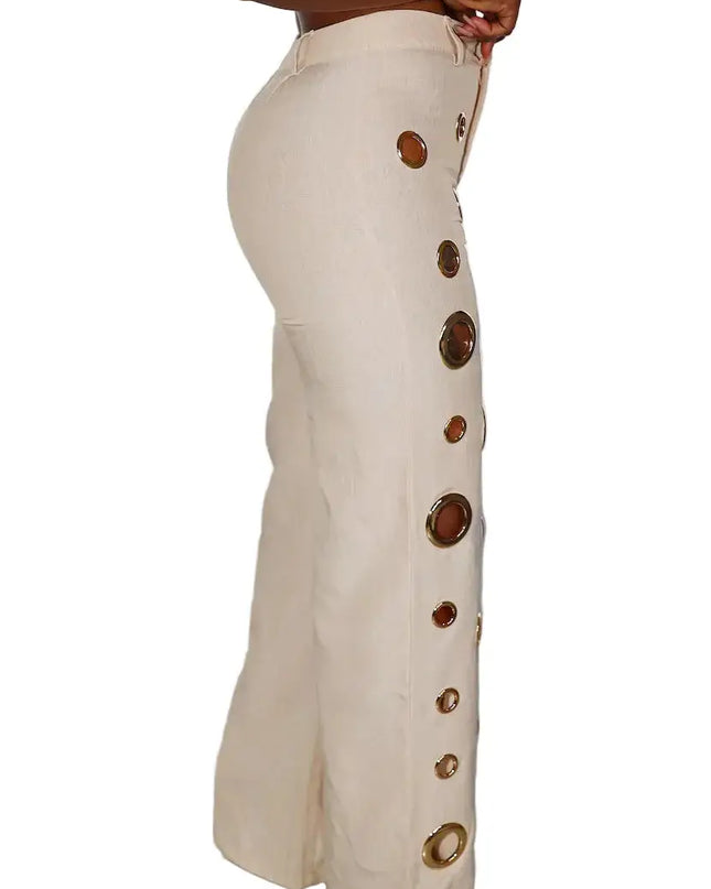 Beige pants with decorative buttons worn by a person against a white curtain background