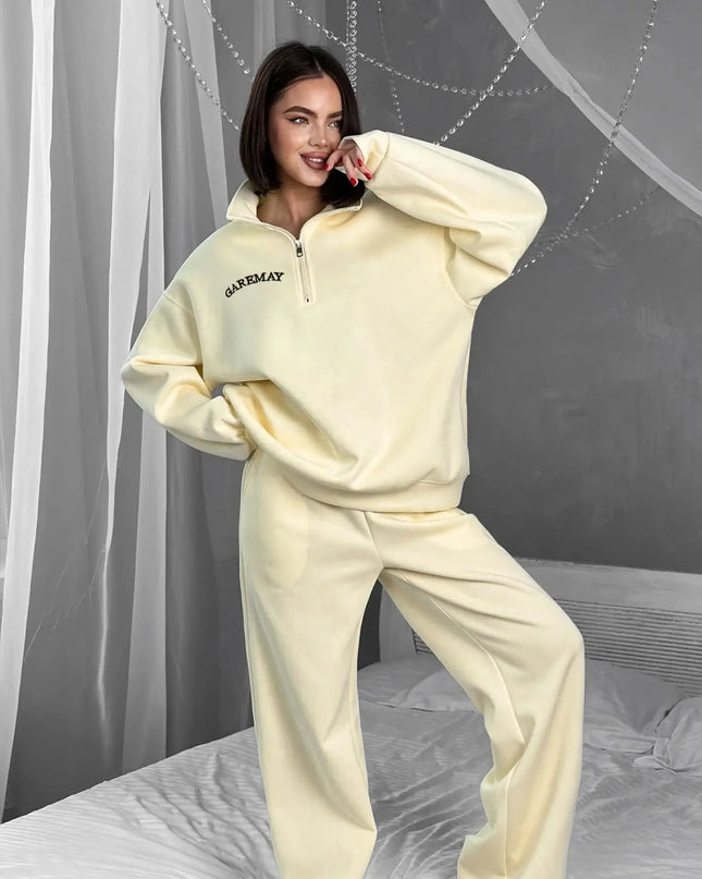 Woman wearing a cream-colored tracksuit with 'Ganni' branding in a bedroom setting.