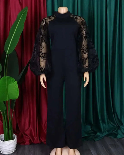Black outfit with sheer sleeves on a mannequin against red and green draped curtains.