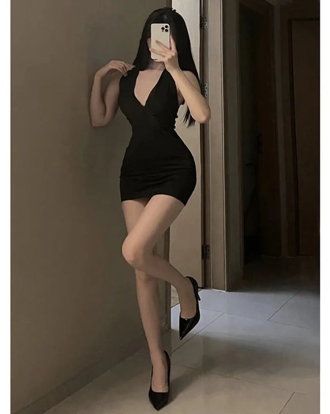 Woman taking a mirror selfie wearing a black dress and high heels in a room.