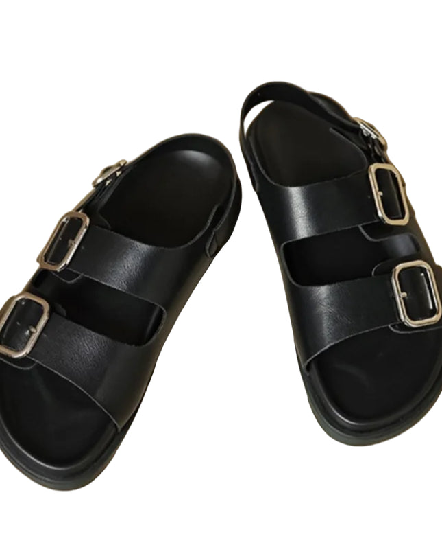 Black sandals with gold buckles on a beige surface
