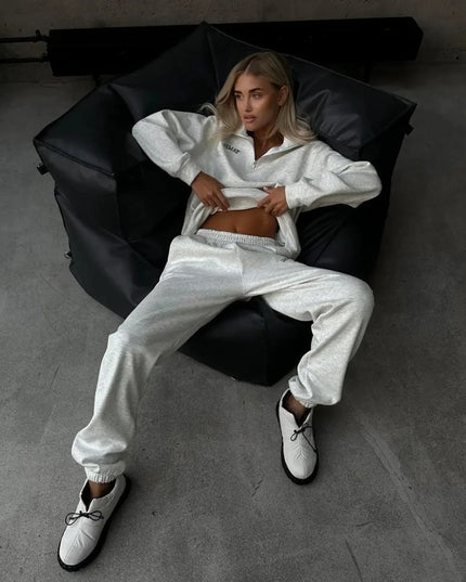 Person wearing a white tracksuit sitting on a black bean bag chair in a minimalistic room.