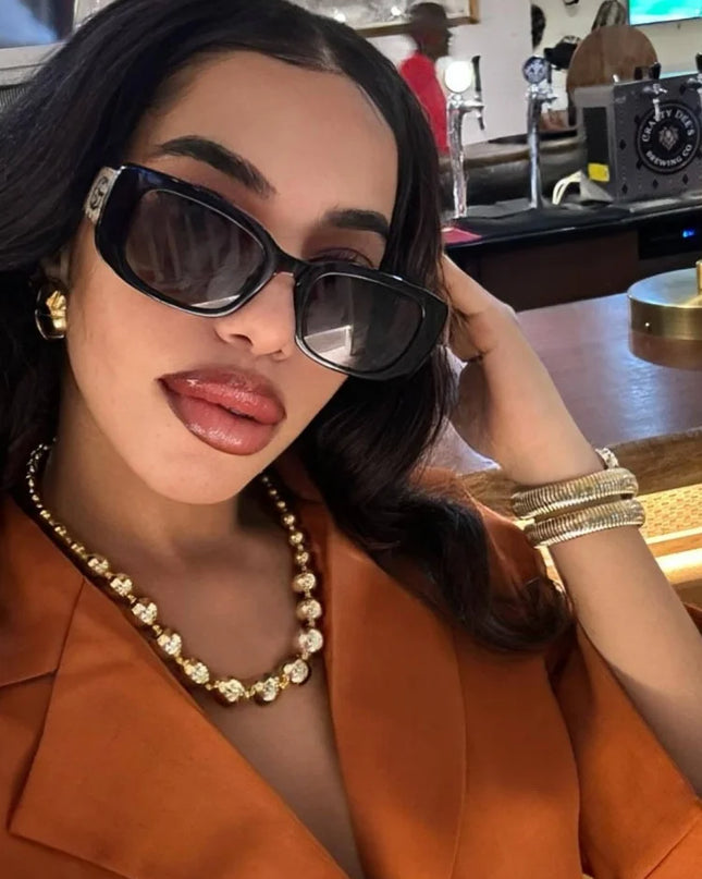 Woman wearing stylish sunglasses and a gold necklace in a chic setting.