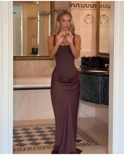 Model in a brown pleated maxi dress posing in an elegant bathroom setting, showcasing its sophisticated style.