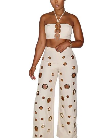 Woman wearing a strapless top and wide-leg pants with cut-out design against a white curtain background.