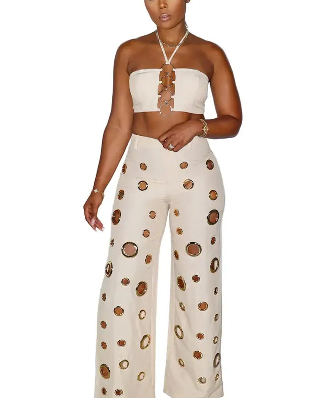 Woman wearing a strapless top and wide-leg pants with cut-out design against a white curtain background.