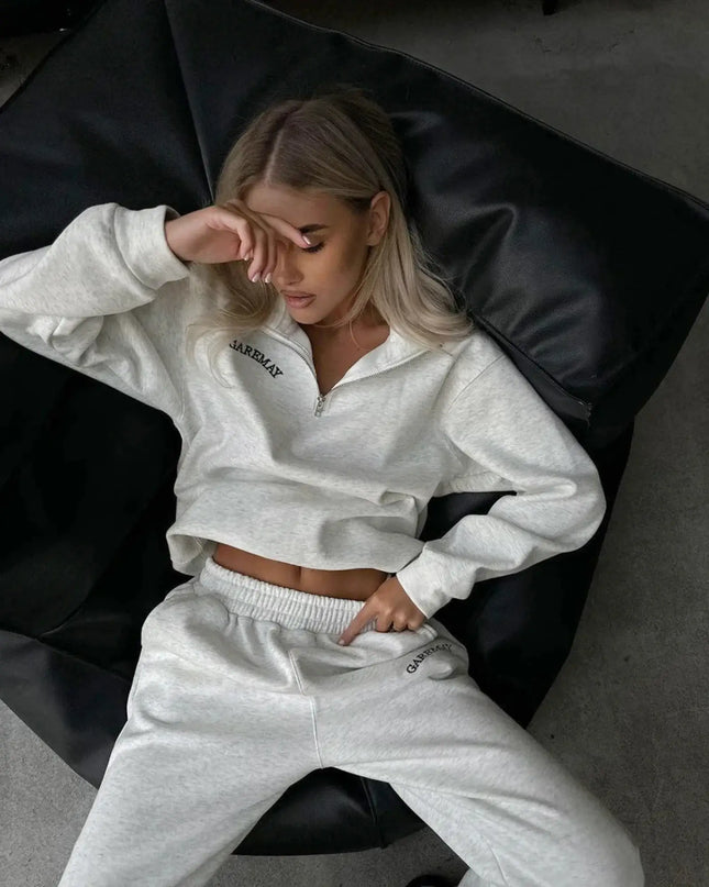 Woman wearing a gray sweatshirt and pants with a brand logo, sitting on a black bean bag chair.
