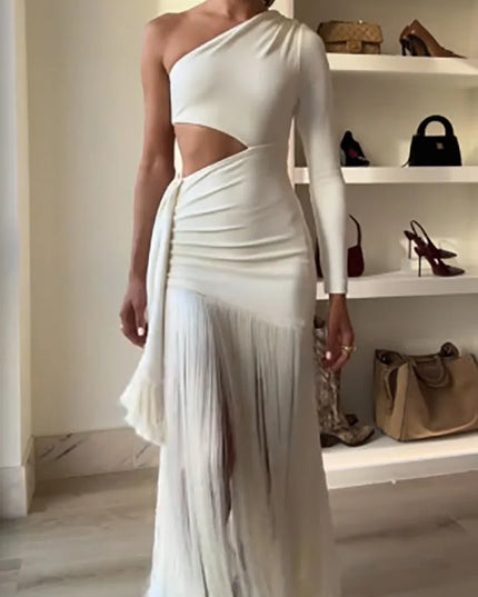 Woman wearing a white one-shoulder dress with cut-out design in a room with shelves displaying bags.